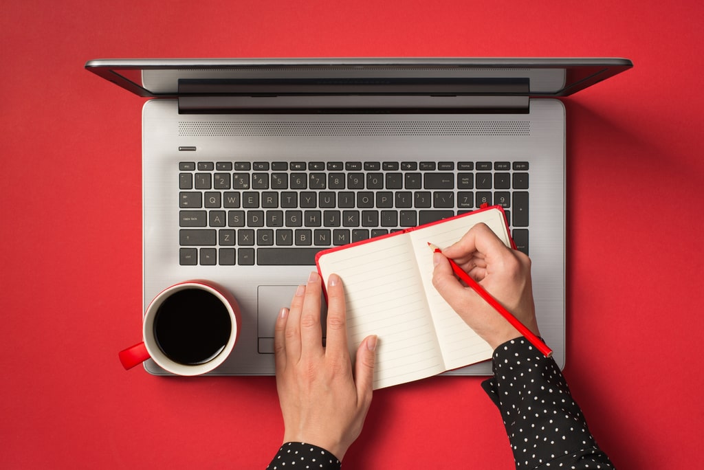 Il blog è un altro formidabile alleato per costruire la propria brand awareness. Articoli seo, su contenuti di qualità, possono aiutare il proprio marchio a posizionarsi sui motori di ricerca. Nella foto la vista di un laptop dall'alto con mani che scrivono su un taccuino.