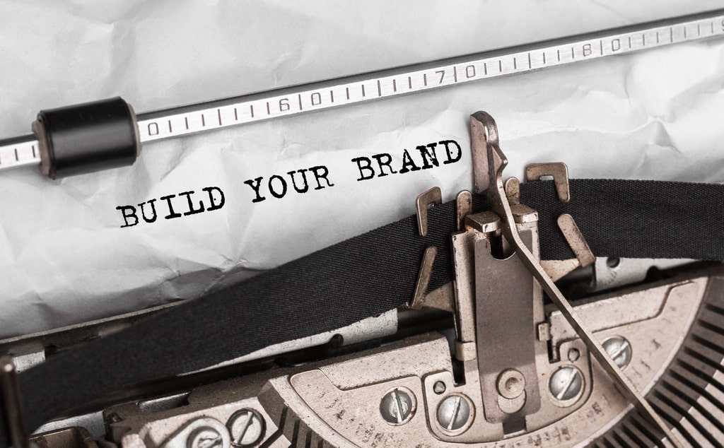 Fare storytelling è uno dei modi migliori per accrescere la propria brand awareness: si tratta di parlare della storia e dei valori della propria azienda servendosi di tecniche narrative. Nella foto, una macchina da scrivere con la scritta build tour brand su un foglio.